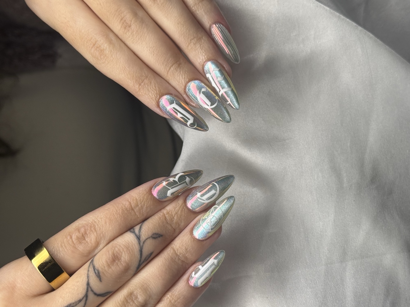 Long almond nails in holographic chrome with pastel swirls and white gothic initials