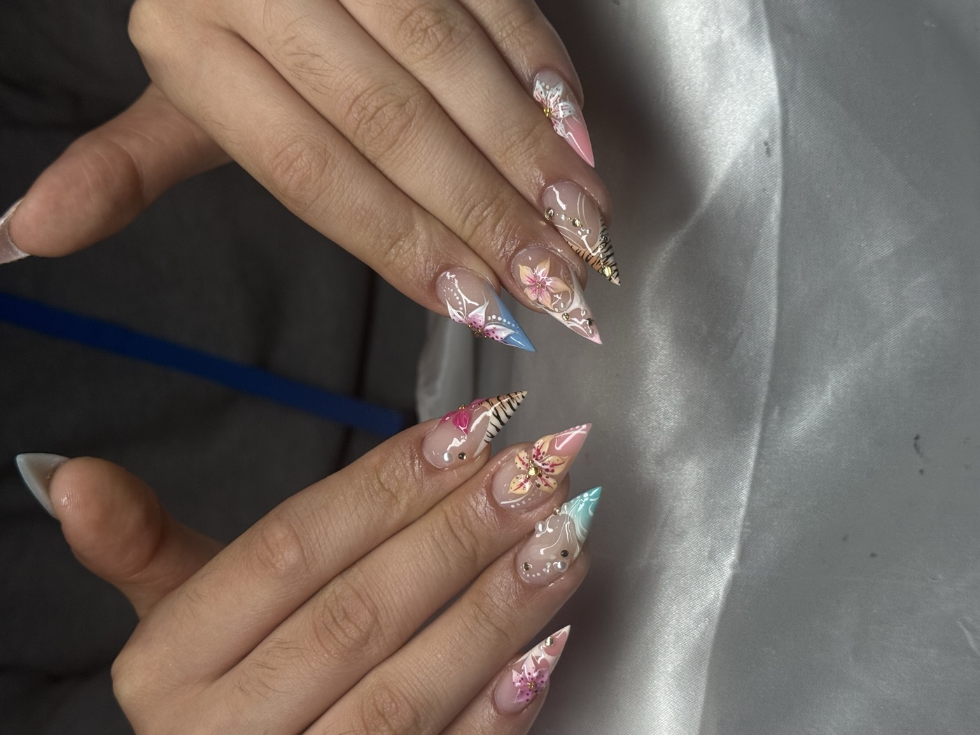 Sheer stiletto nails with sculpted 3D pink and blue florals, gold foil and rhinestones
