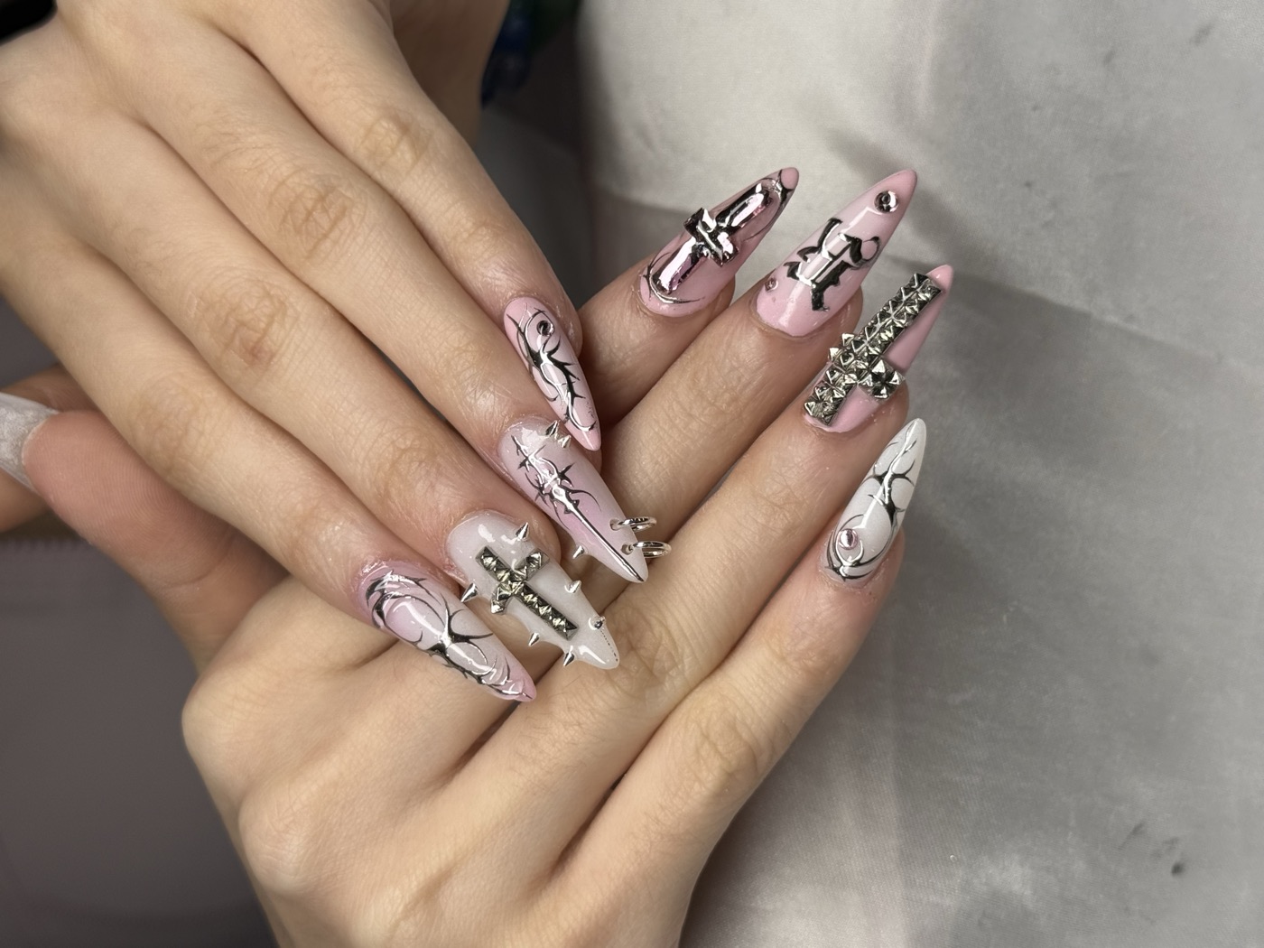 Pink and white stiletto nails with 3D silver cross charms, rhinestones and dangles